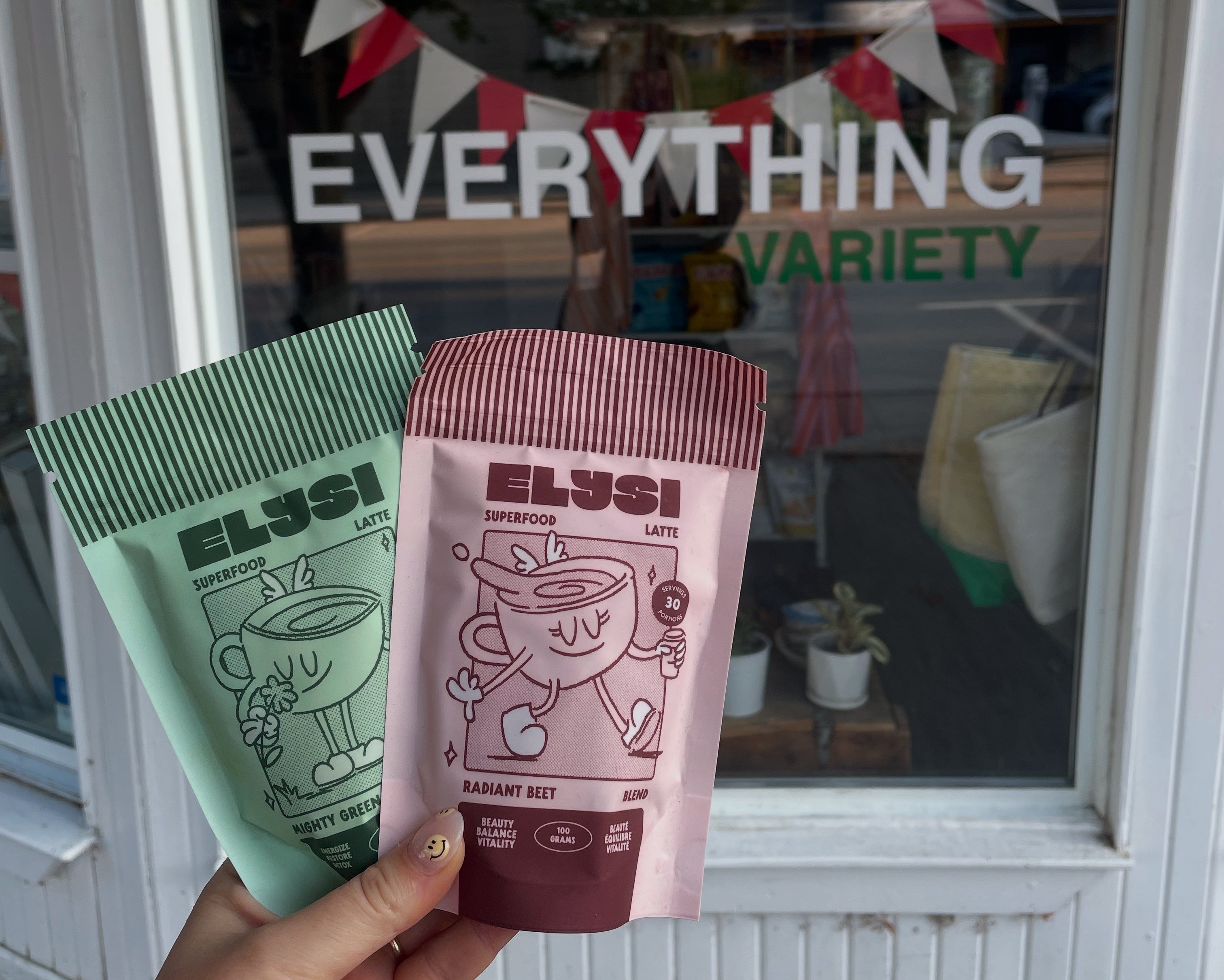 Two ELYSI food product packets held in front of a store window with 'Everything Variety' sign.